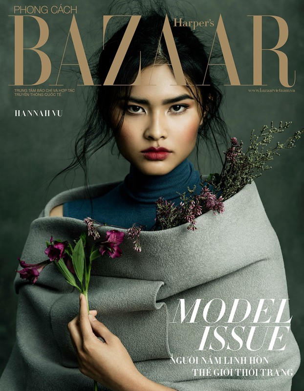 Magazine cover featuring an adult female model. She is holding purple flowers, partially wrapped in a grey coat, and wearing a blue top.