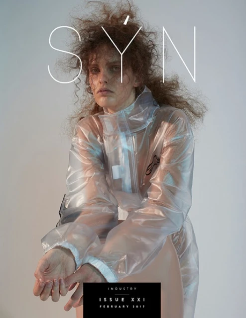 Fashion magazine cover featuring a model in a transparent jacket with tousled hair, set against a neutral backdrop with bold typography.