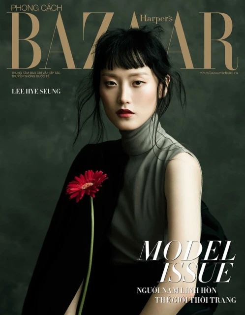 Harper's Bazaar magazine cover featuring an Asian woman model in a gray top and black jacket holding a red gerbera daisy.