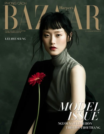 Harper's Bazaar magazine cover featuring an Asian woman model in a gray top and black jacket holding a red gerbera daisy.