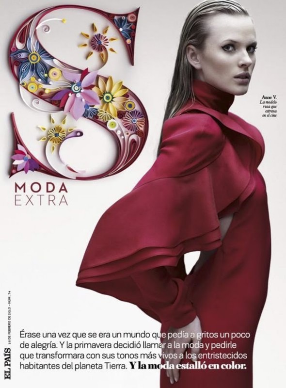 Fashion editorial shot of a blonde woman in a red coat posing next to a decorative letter 'S' in a studio setting.