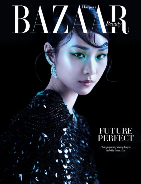 Close-up magazine cover of a woman with green eye makeup and large crystal earrings, wearing a dark sequined top against a black background.