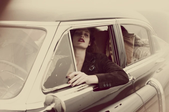 Woman in dark jacket leaning out of the window of a vintage car with sepia-toned grading