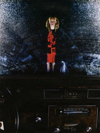 A young child stands in the rain behind a car windshield, viewed from inside the vehicle with a dark, moody atmosphere.