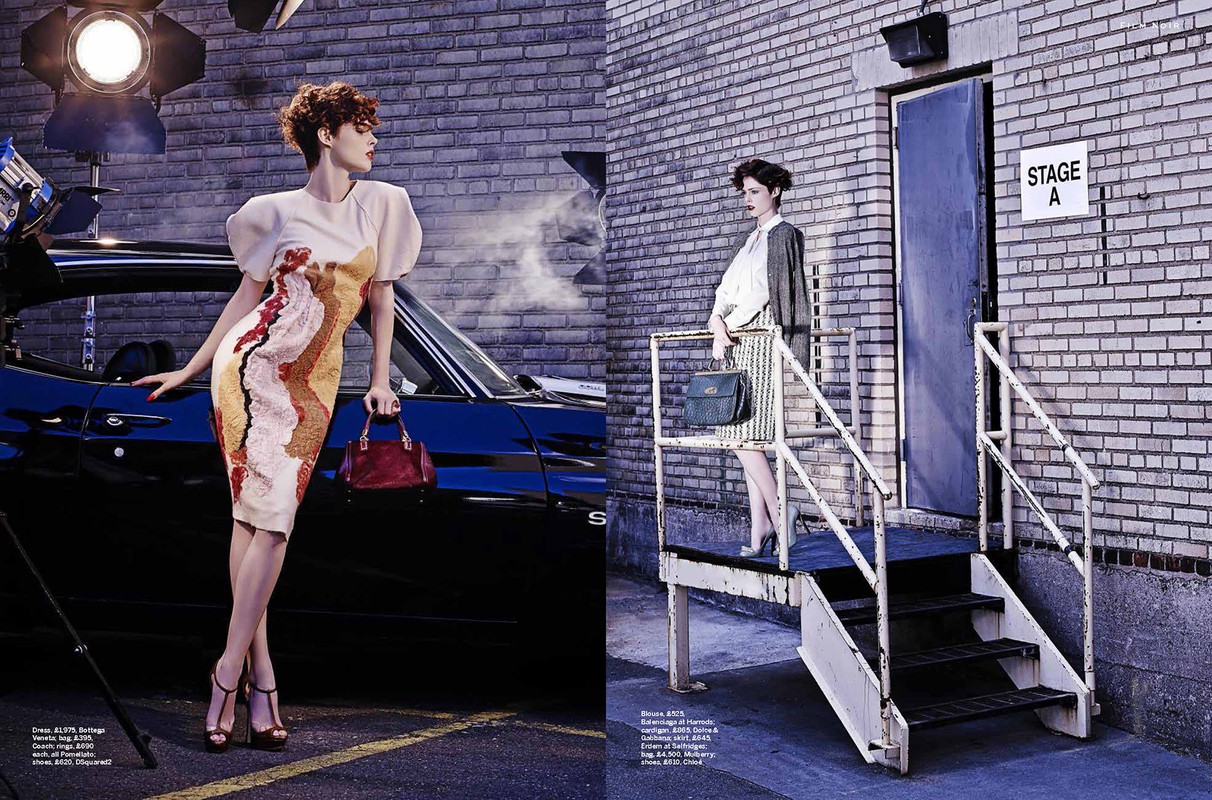 Fashion editorial featuring two female models posing near a car and a building with a door and stairs, lit by studio lights.