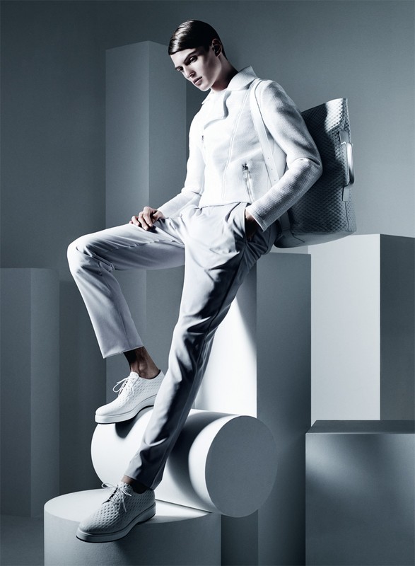 Model in white jacket and trousers posing on geometric studio blocks with a woven tote bag