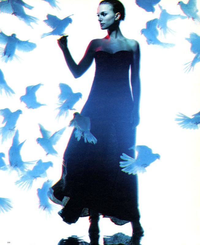 Elegant woman in a dark gown surrounded by white doves in a bright studio setting, creating a surreal and graceful fashion image.
