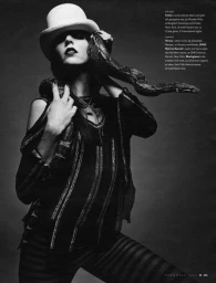 Model wearing a white bowler hat and dark clothing with a snake draped around shoulders against a dark background