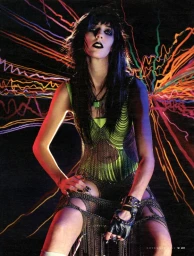 Punk model with dark makeup and black hair wearing green sleeveless chainmail dress with studded leather gloves.