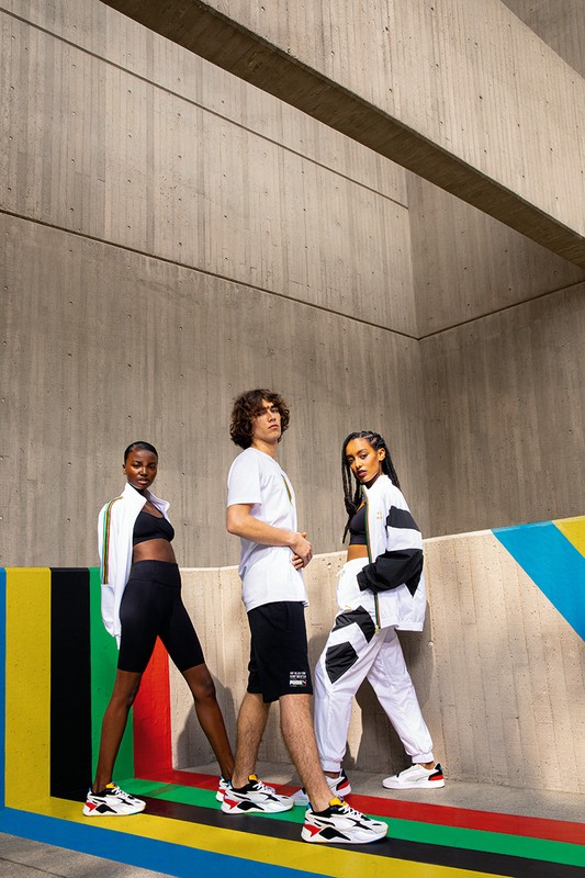 Three diverse young adult models pose together in sportswear against a concrete wall with painted stripes, showcasing a fashion campaign.