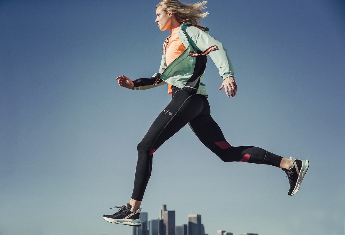 Athletic woman in sportswear leaps against the skyline of Los Angeles in this eye-level, medium shot. Bright color accents.