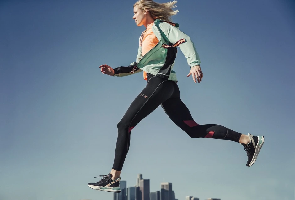 Athletic woman in sportswear leaps against the skyline of Los Angeles in this eye-level, medium shot. Bright color accents.