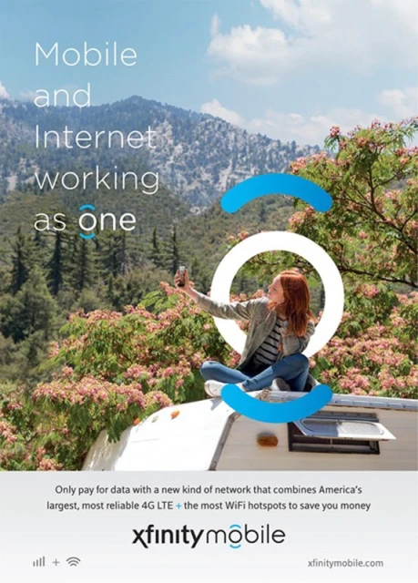 A red-haired woman sits atop a white RV against a mountain backdrop, taking a selfie with her cell phone in an Xfinity Mobile advertisement.
