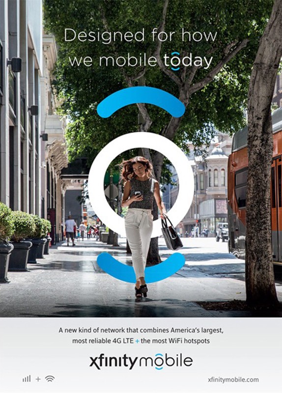 Woman walks on city sidewalk in Xfinity Mobile advertisement, holding cell phone and bag, with green trees and white building facades.