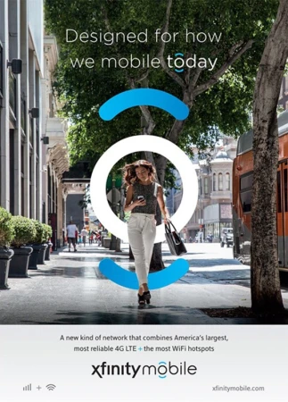 Woman walks on city sidewalk in Xfinity Mobile advertisement, holding cell phone and bag, with green trees and white building facades.