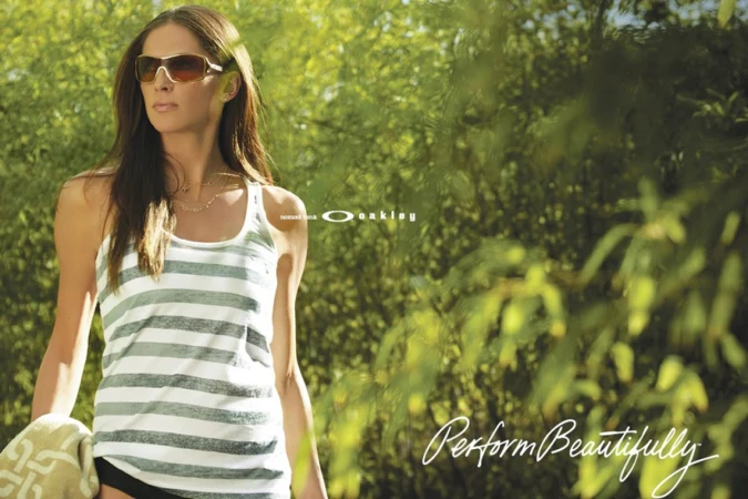 Woman wearing sunglasses and striped tank top holding a towel outdoors with foliage