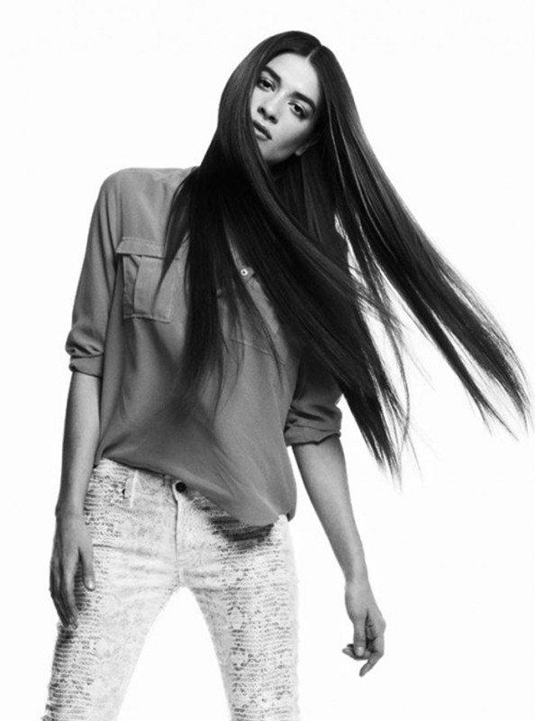 Monochrome portrait of a woman with long dark hair, wearing a collared shirt and patterned jeans, posing against a white background.