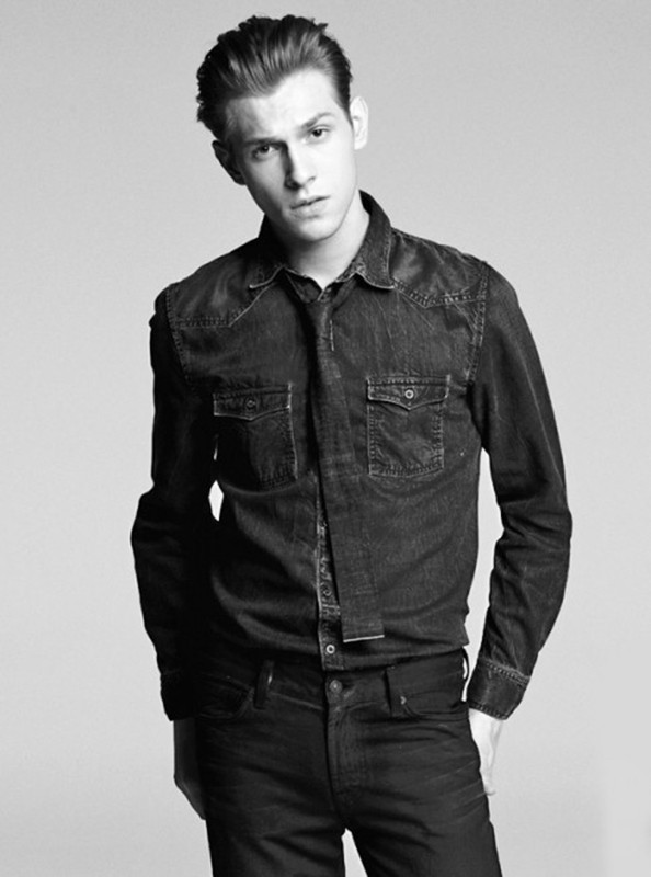 Monochrome portrait of a young adult man in a dark denim shirt and jeans posing in a studio. Fashion shot with studio lighting.