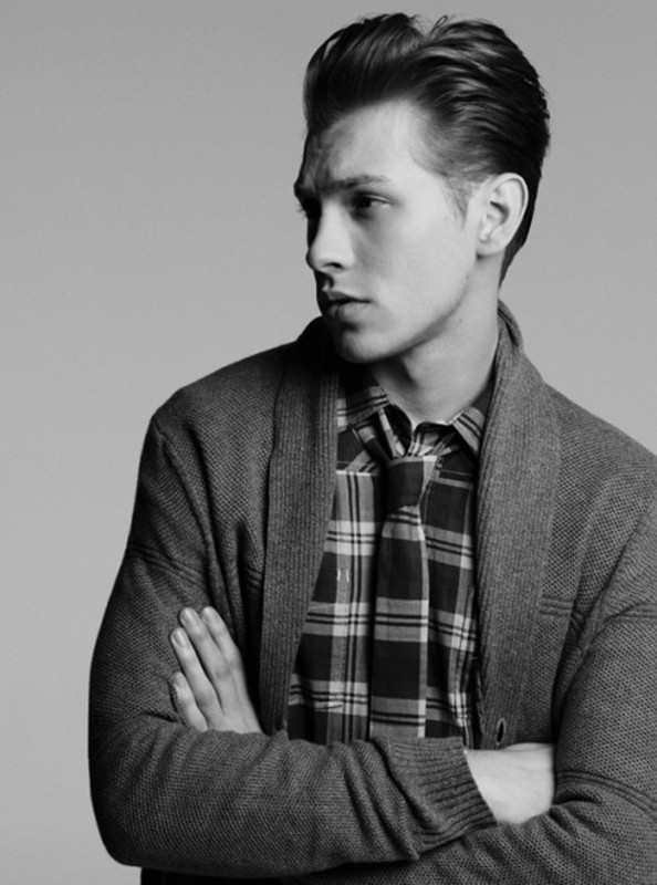 Monochrome portrait of a handsome adult man in a cardigan sweater, posing indoors with a neutral background. Fashionable look.