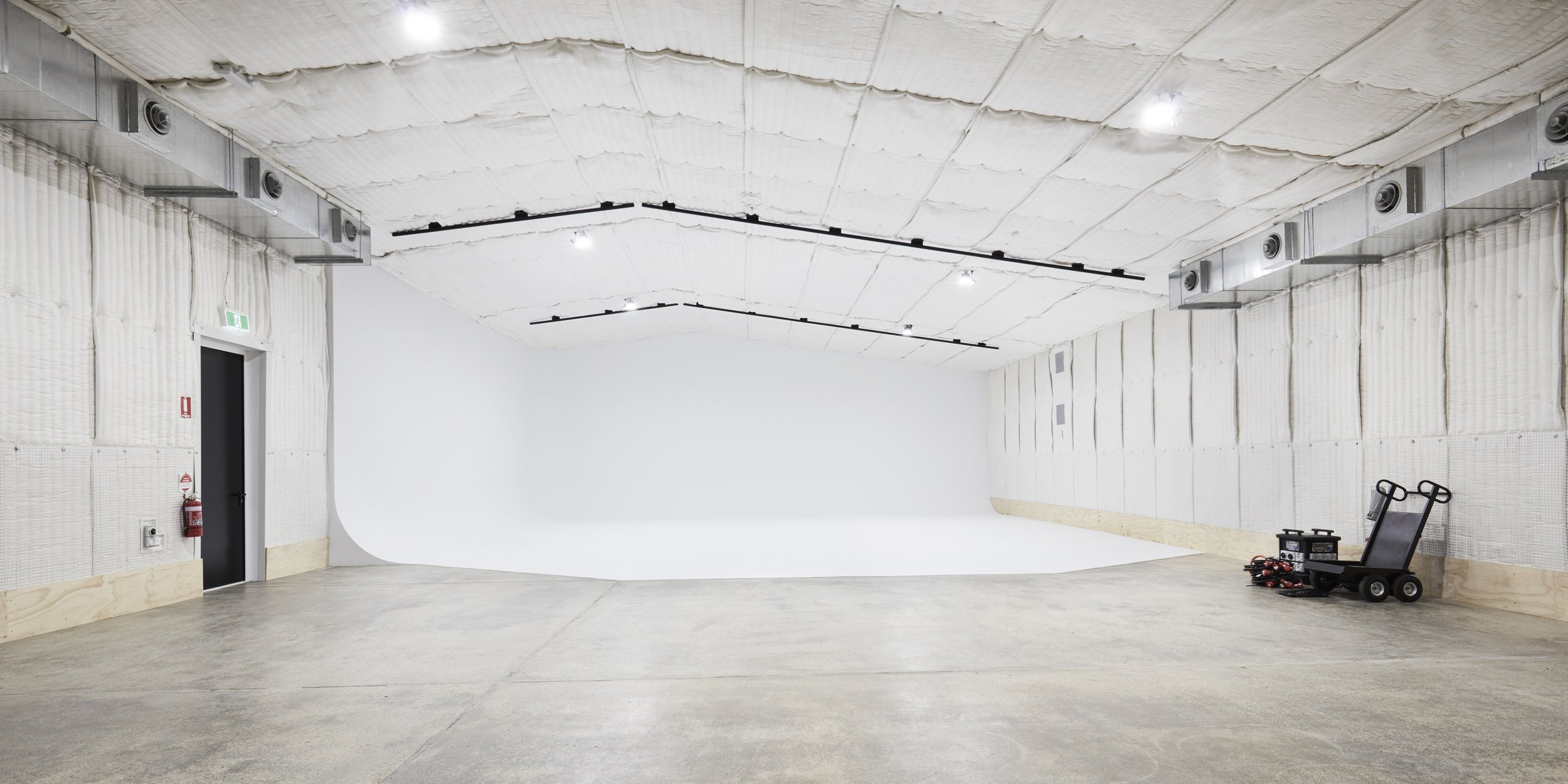 Spacious, empty photo studio with white backdrop, grey concrete floor, and industrial lighting. Interior photography of a creative workspace.