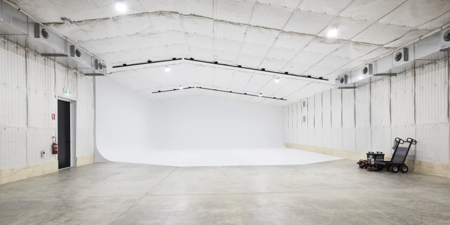Spacious, empty photo studio with white backdrop, grey concrete floor, and industrial lighting. Interior photography of a creative workspace.