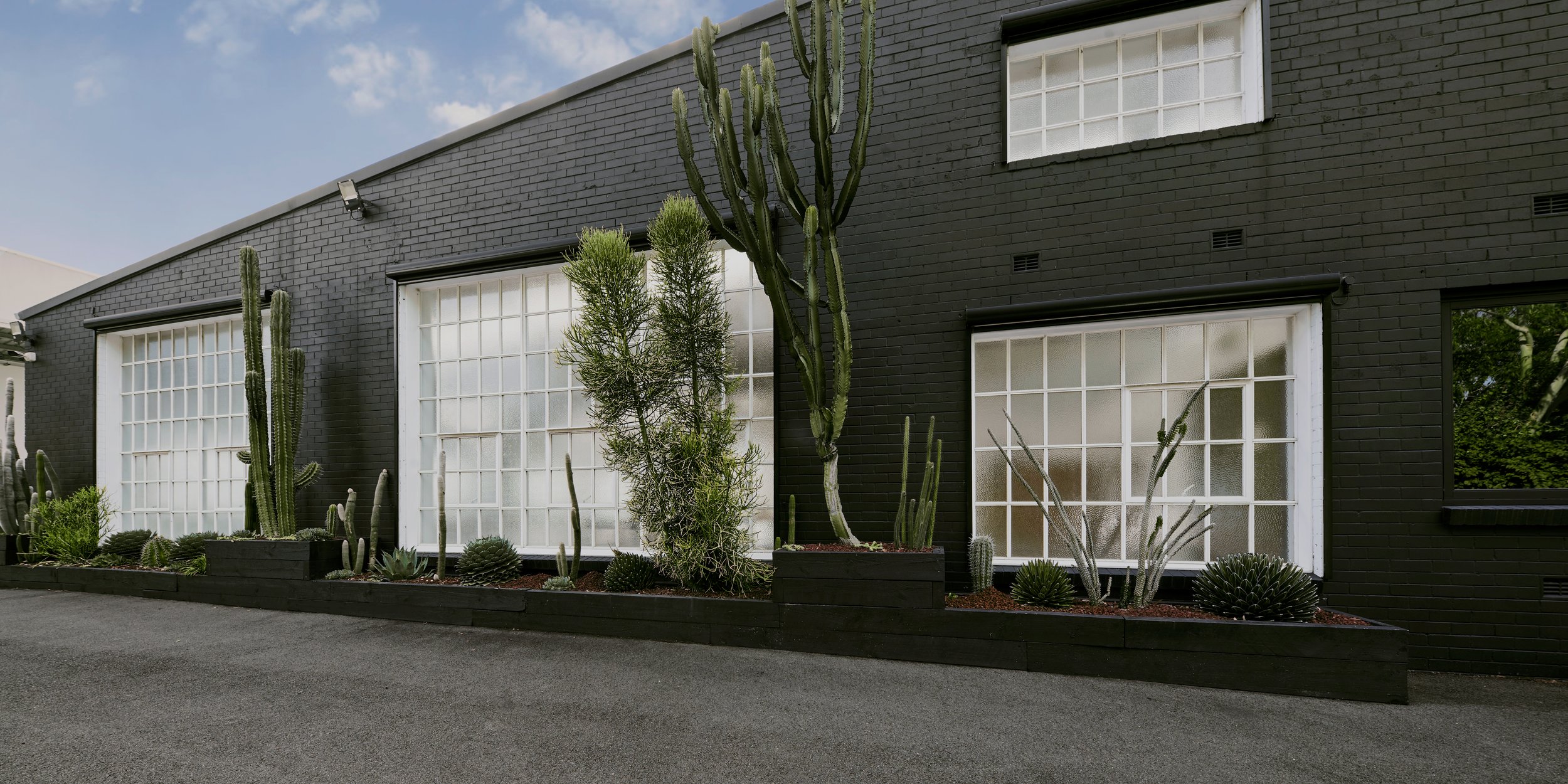 Exterior of a dark brick building with large windows and potted cactus plants in front, showcasing modern architecture and landscaping.