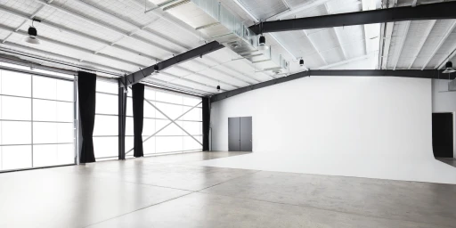 Wide interior view of Baker Street Studios in Sydney showing a large white seamless curve, exposed beams, and industrial windows.