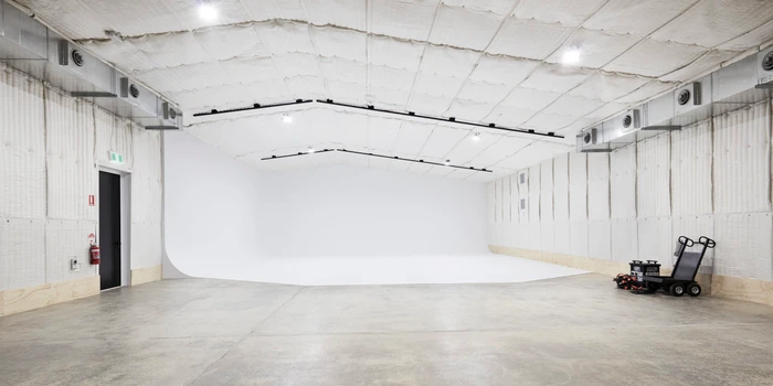 Empty photo studio interior featuring a large white cyclorama wall, concrete floor, and exposed ductwork.