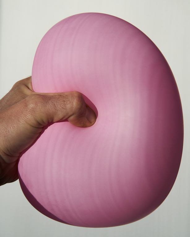 Close-up of a hand squeezing a pink balloon against a white background, showcasing texture and form under studio lighting.