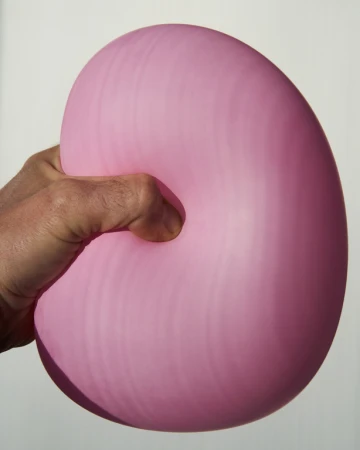 Close-up of a hand squeezing a pink balloon against a white background, showcasing texture and form under studio lighting.