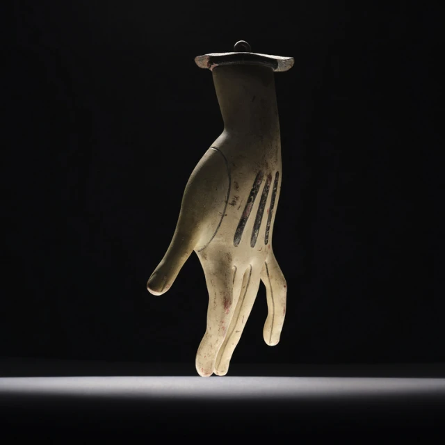 A surreal still life of a sculptural hand with black stripes, suspended against a dramatic black background with spotlight lighting.