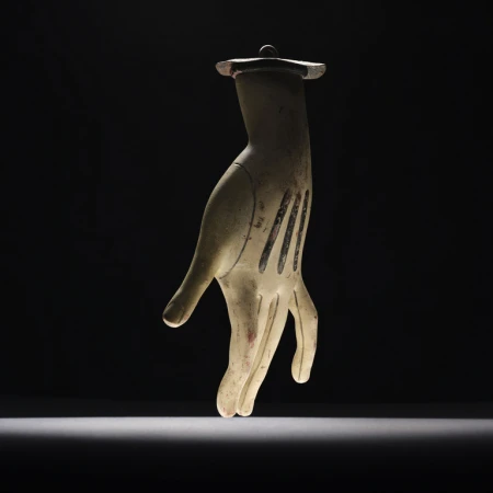 A surreal still life of a sculptural hand with black stripes, suspended against a dramatic black background with spotlight lighting.