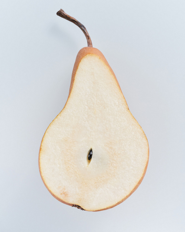 Close-up studio shot of a halved pear showing its seed, peel, and stem; clean, minimal food photography against white.