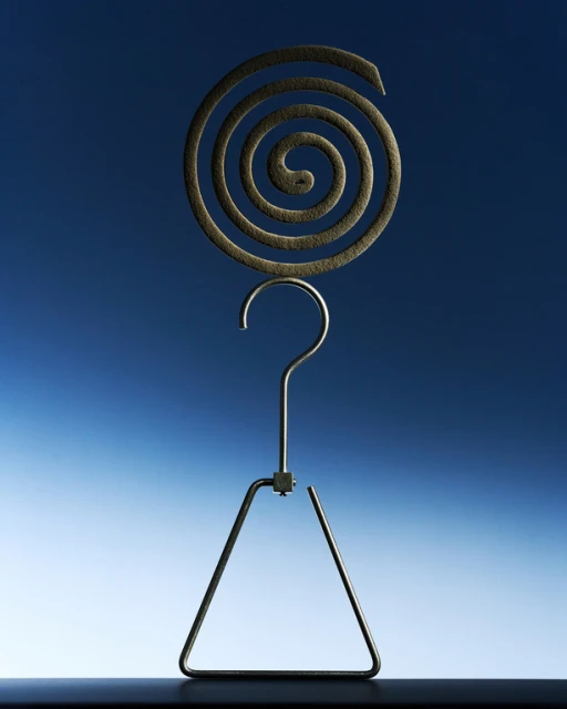 Elevated view of an insect repellent coil, a silver-colored metal holder, and a dark table against a gradient blue background.