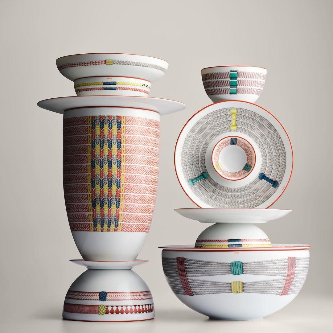 Stack of ceramic bowls, plates, and vase featuring colorful decorative geometric patterns displayed against a neutral background.