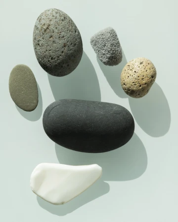A collection of grey, black, white, and tan smooth rocks and stones with varying shapes and sizes arranged on a light blue surface.