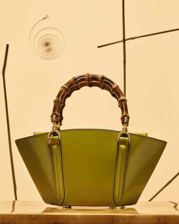 Gucci handbag with bamboo handle displayed on a wooden surface against a patterned beige background in a studio setting.