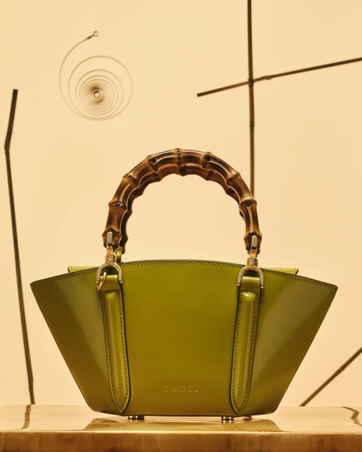 Gucci handbag with bamboo handle displayed on a wooden surface against a patterned beige background in a studio setting.