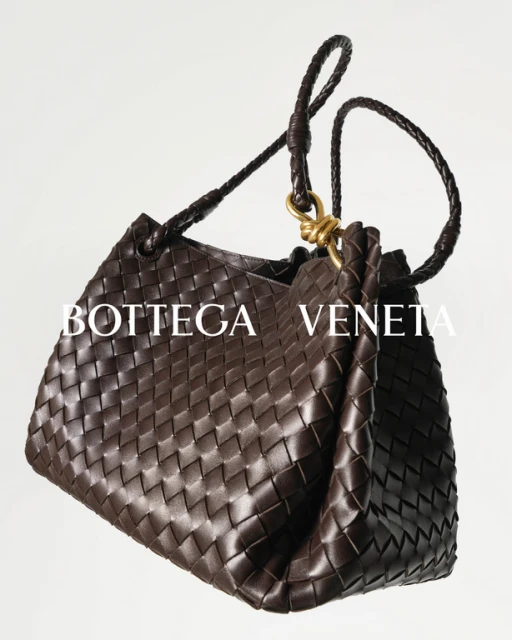 Elevated studio shot of a woven brown leather Bottega Veneta purse with a short woven handle against a light backdrop.