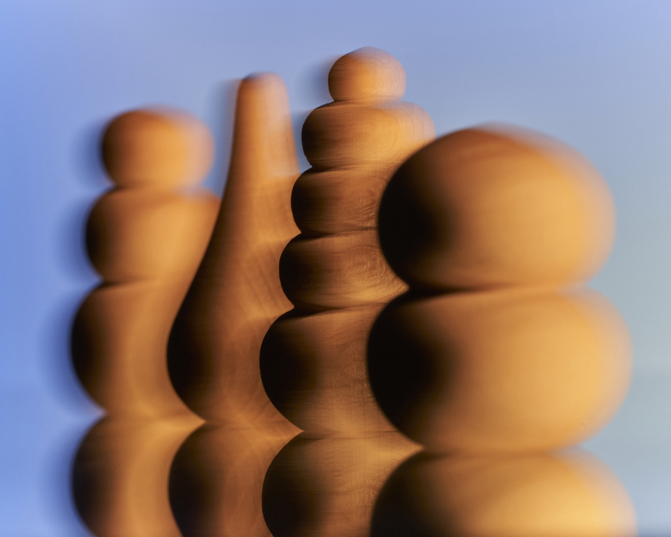 Abstract view of four wooden, rounded sculpture pieces in a row, with reflections on a shiny surface against a blue gradient background.