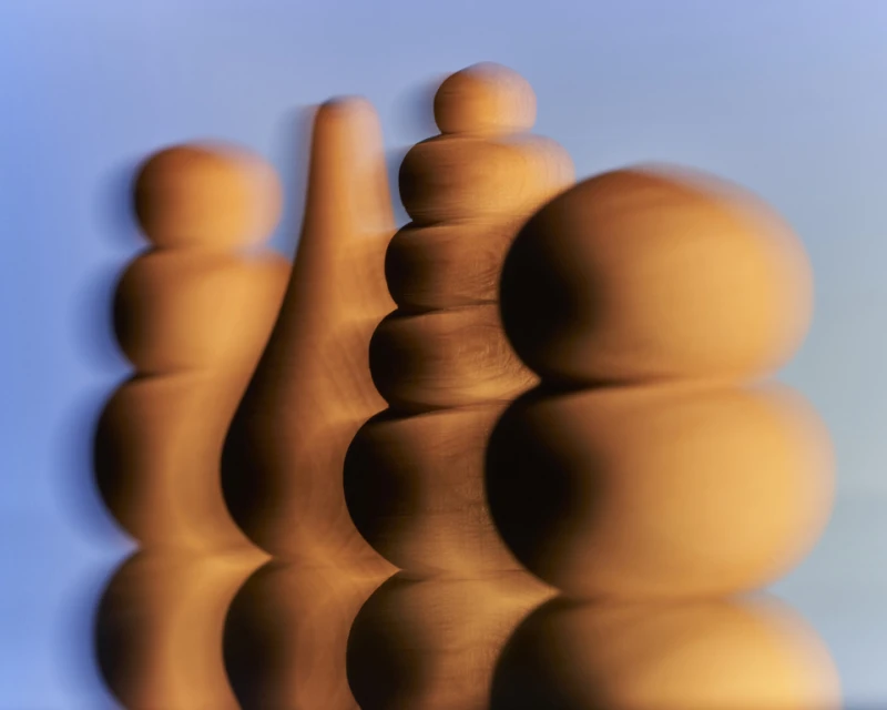 Abstract view of four wooden, rounded sculpture pieces in a row, with reflections on a shiny surface against a blue gradient background.