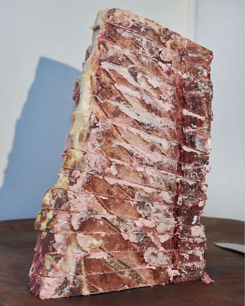 Large cut of raw beef featuring visible marbling and bone structure, displayed on a dark wood surface with a white background.