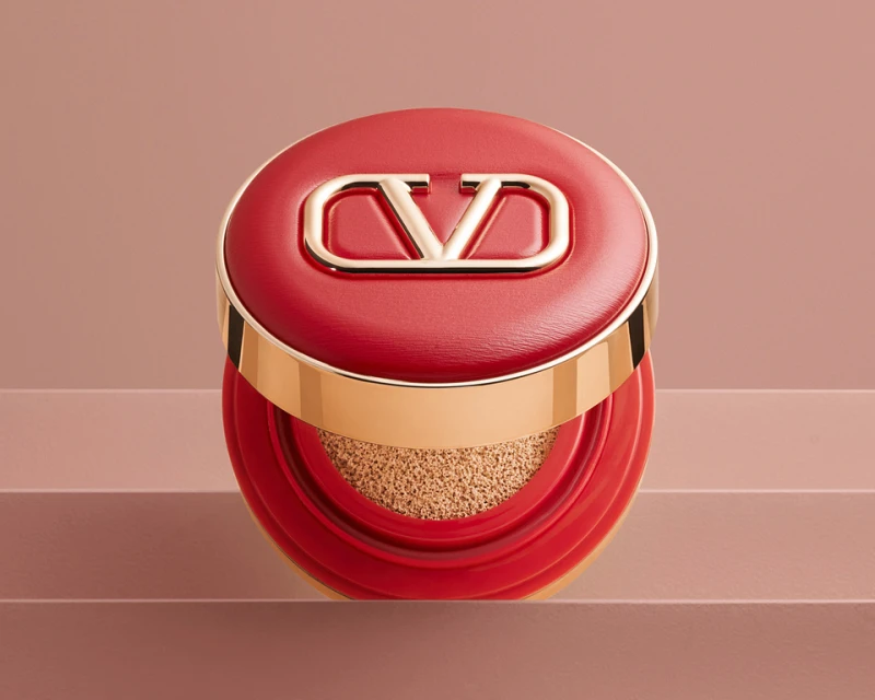 Red and gold Valentino cushion compact with logo on a layered pale pink background, showing the makeup product's design.