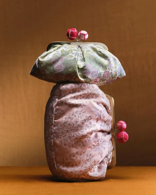 Stacked floral print kiss-lock closure clutch purses in pink and green on a gradient brown backdrop. Fashion accessory still life.