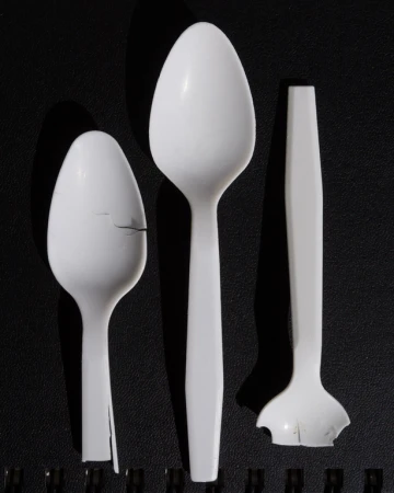 Studio shot of three damaged white plastic spoons of different sizes against a black background, showcasing wear and breakage.