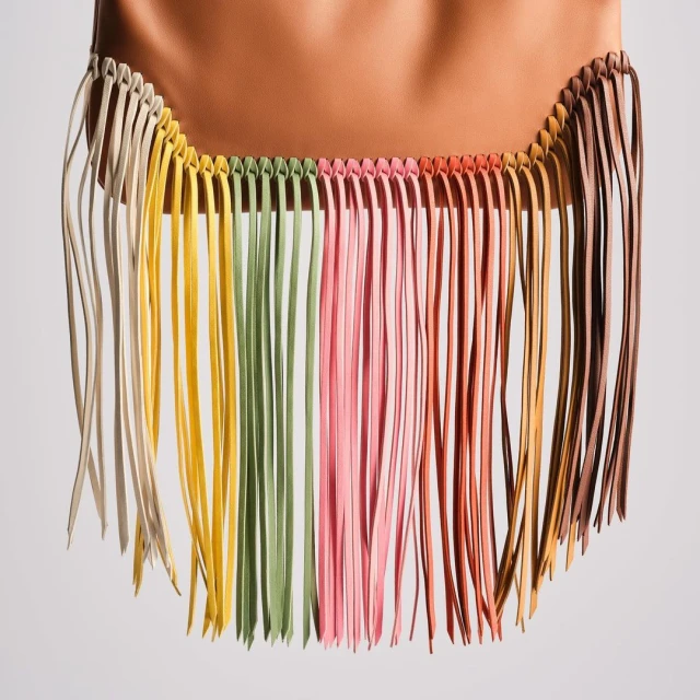 Tan-colored bag with rainbow-colored fringe, crafted from leather, hanging against a neutral backdrop in a studio setting with soft lighting.