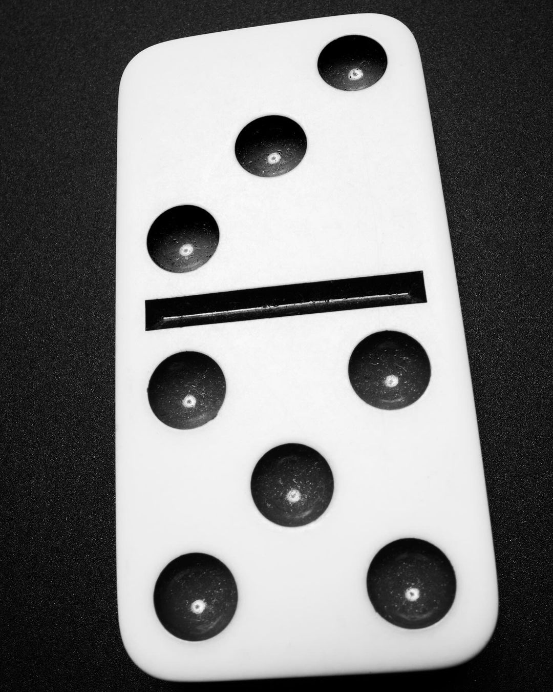 Close-up black and white studio shot of a single, white, rectangular domino piece with black dots showing a five-one split.
