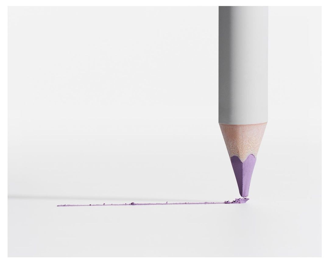 Close-up of a lilac-tipped pencil on white background, drawing a line and leaving a trail of pigment dust. Minimalist beauty or art concept.