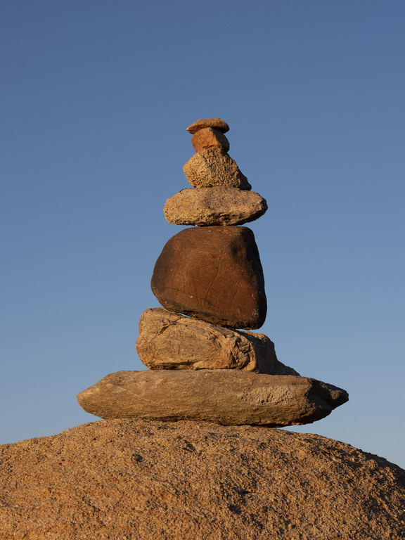 Zen rock stack towers against clear blue sky. Natural rock cairn sculpture on earth, balanced for meditation and peaceful contemplation.