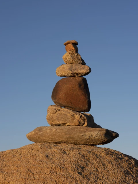 Zen rock stack towers against clear blue sky. Natural rock cairn sculpture on earth, balanced for meditation and peaceful contemplation.